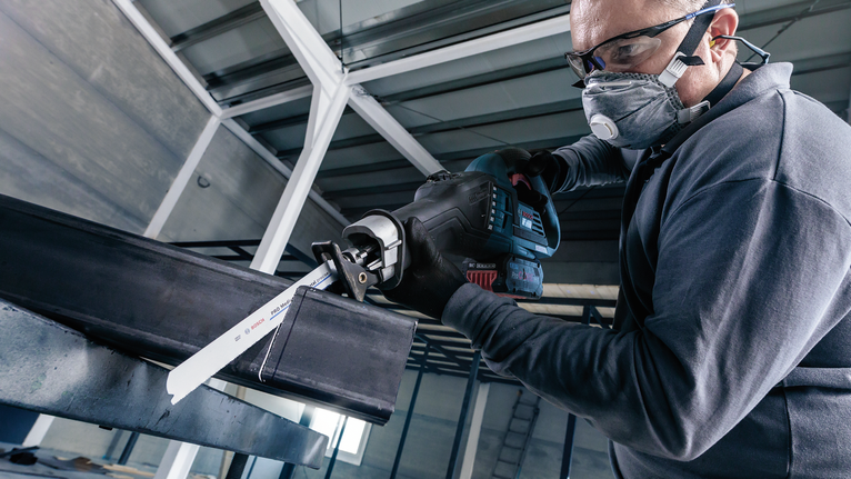 Una persona que usa equipo de seguridad utiliza una sierra alternativa para cortar una viga de acero.