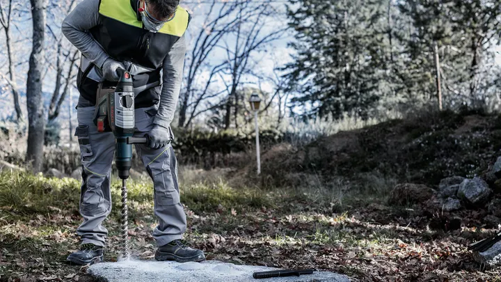 Una persona que usa equipo de seguridad perfora hormigón al aire libre.