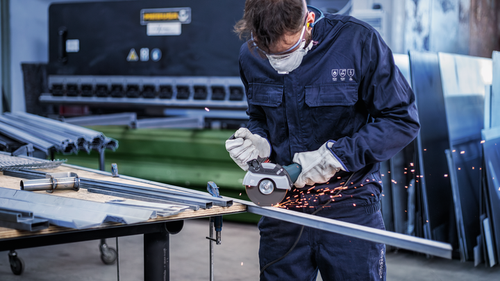Una persona que usa equipo de seguridad utiliza una herramienta de corte en una barra de metal en un taller.