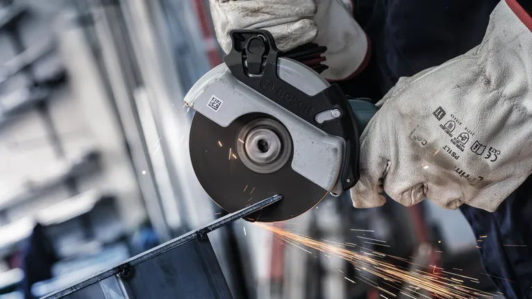 Una persona que usa equipo de seguridad utiliza una amoladora angular para cortar metal, lo que produce chispas.