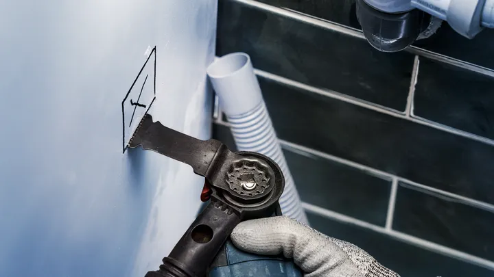 Una persona que usa equipo de seguridad corta una sección marcada de una pared con una herramienta oscilante.