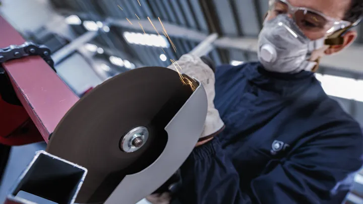 Una persona que usa equipo de seguridad utiliza una herramienta de corte para cortar metal.