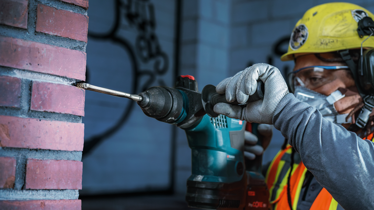 Una persona que lleva equipo de seguridad perfora una pared de ladrillos.