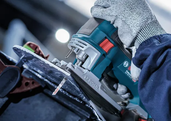 Una persona que usa equipo de seguridad utiliza una sierra caladora para cortar una lámina de material.