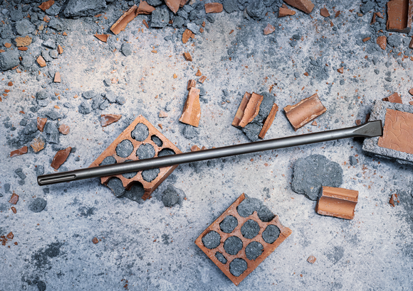 Cincel rodeado de ladrillos rotos y escombros de hormigón en un sitio de construcción.