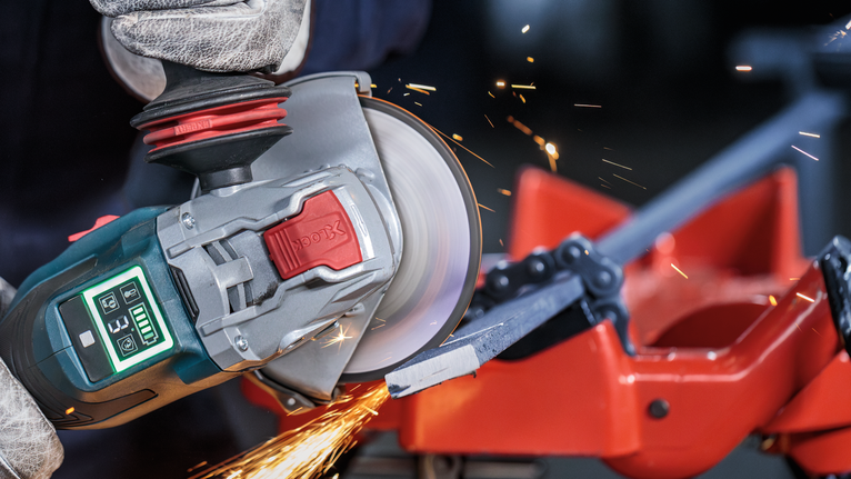 Una persona que usa equipo de seguridad utiliza una amoladora angular para cortar una barra de metal.