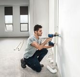 Una persona perfora una pared para instalar tuberías en una habitación luminosa y sin terminar.