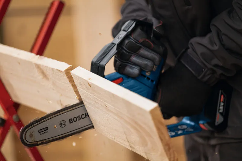 Una persona que usa equipo de seguridad utiliza una sierra podadora inalámbrica para cortar una tabla de madera.