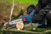 Una persona que usa equipo de seguridad utiliza una sierra podadora inalámbrica para cortar la rama de un árbol.