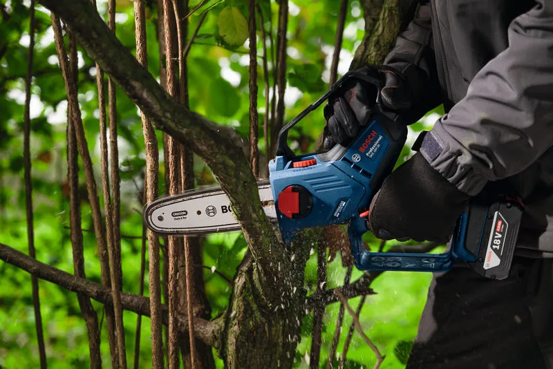 Una persona que usa equipo de seguridad utiliza una sierra podadora inalámbrica para cortar la rama de un árbol.