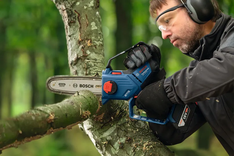 Una persona que usa equipo de seguridad corta la rama de un árbol con una podadora inalámbrica.