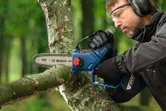 Una persona que usa equipo de seguridad corta la rama de un árbol con una podadora inalámbrica.