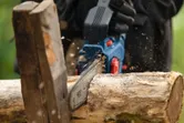 Una persona que usa equipo de seguridad utiliza una sierra podadora inalámbrica para cortar un tronco.