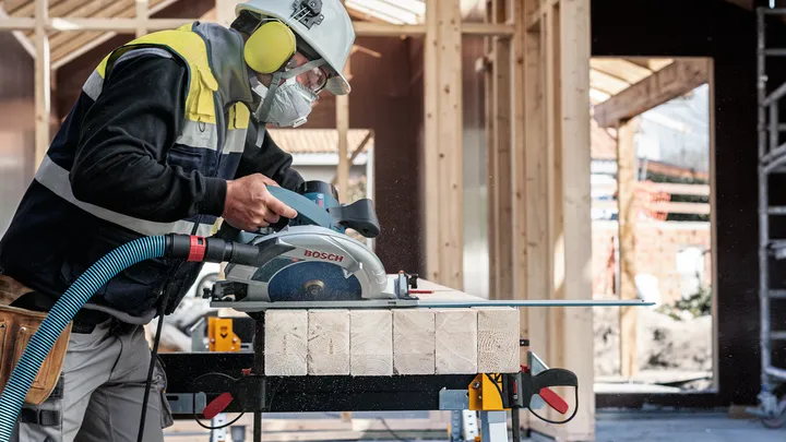Una persona que lleva equipo de seguridad corta madera con una sierra circular en una obra en construcción.