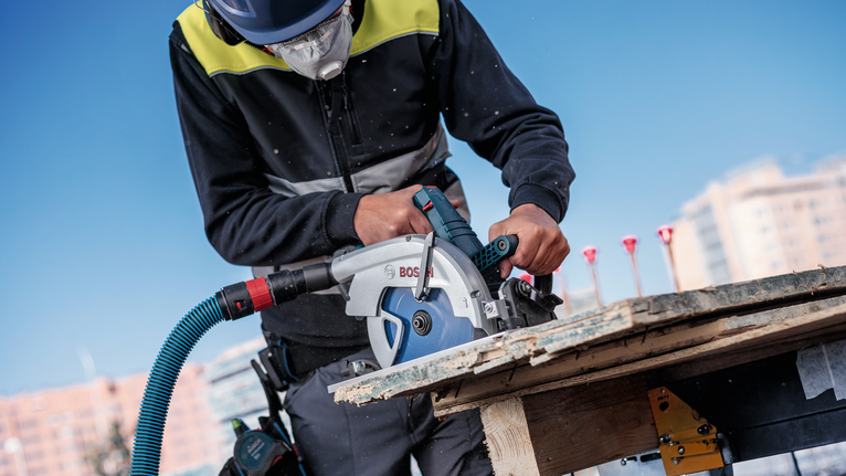 Una persona que lleva equipo de seguridad maneja una sierra circular para cortar tablas de madera.