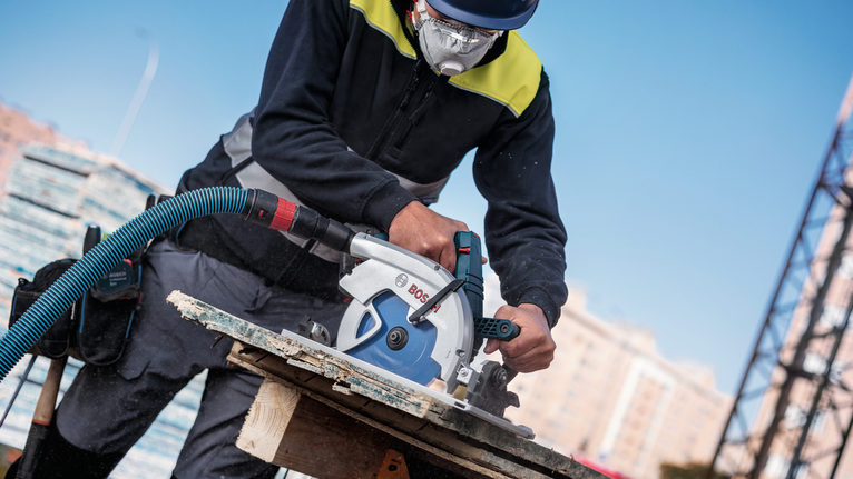 Una persona que lleva equipo de seguridad utiliza una sierra circular para cortar madera en una obra en construcción.