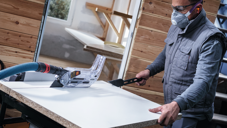Una persona que lleva equipo de seguridad utiliza una sierra de mesa para cortar un panel blanco.