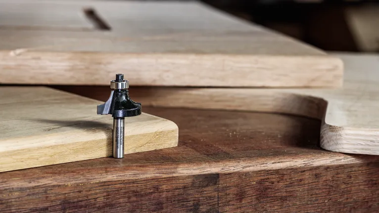 Broca de enrutador apoyada sobre un banco de trabajo de madera al lado de paneles de madera cortados y dados forma.