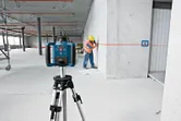 Un trabajador, equipado con material de seguridad, alinea una pared utilizando un nivel láser montado sobre un trípode.