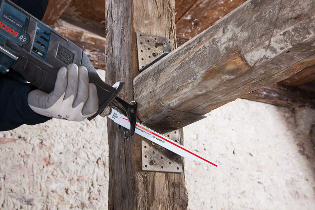 Ein Arbeiter mit Sicherheitsausrüstung schneidet mit einer Säbelsäge einen Holzbalken.