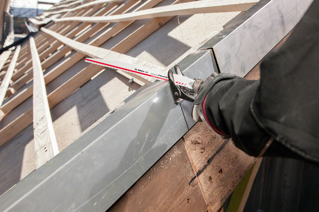 Ein Arbeiter mit Sicherheitsausrüstung schneidet mit einer Säbelsäge einen Metallträger durch.