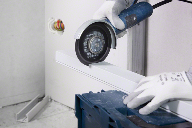 Ein Arbeiter mit Sicherheitsausrüstung schneidet mit einem Winkelschleifer einen Metallkanal.