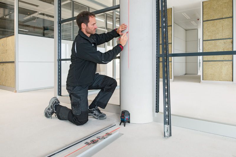 Eine Person in Arbeitskleidung markiert eine Säule mit einem Lasernivelliergerät.