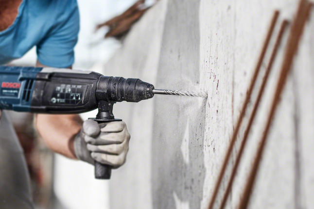 Person mit Sicherheitsausrüstung bohrt in eine Betonwand.