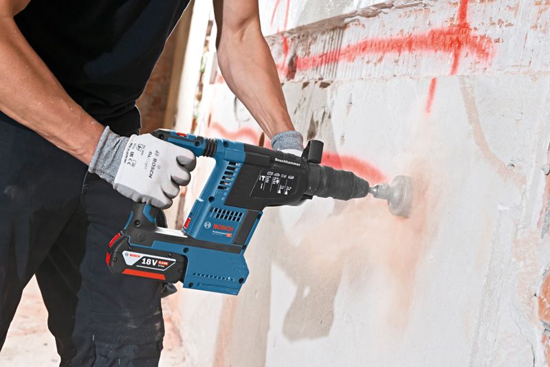 Eine Person mit Schutzausrüstung bohrt mit einem Akku-Bohrhammer in eine Betonwand.