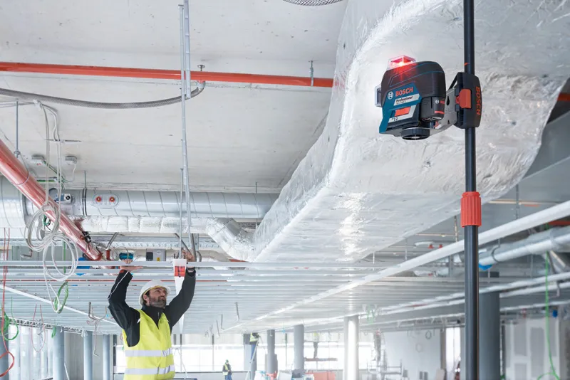 Eine Person mit Sicherheitsausrüstung richtet Deckenrahmen mit einem Lasernivelliergerät aus.