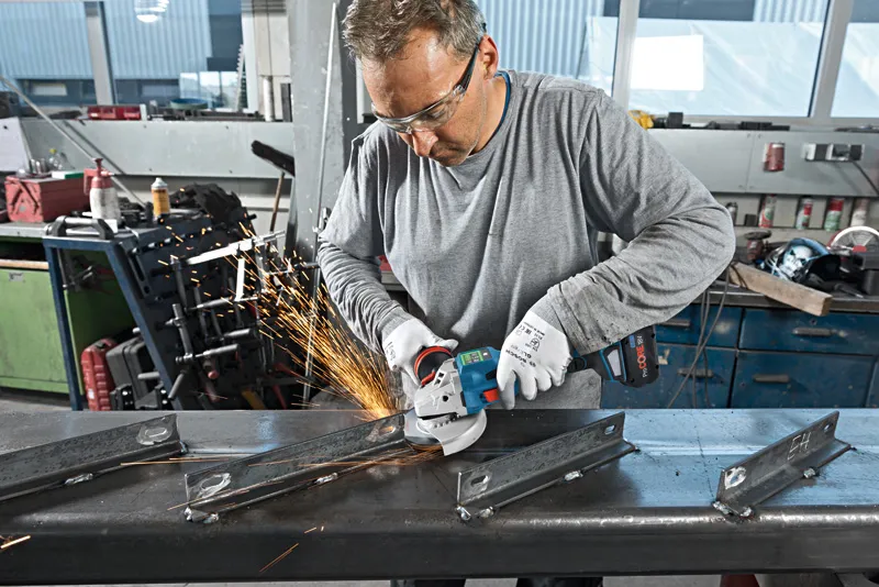 Eine Person mit Sicherheitsausrüstung schneidet mit einem Winkelschleifer einen Metallträger.