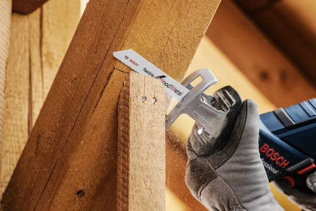 Eine Person, die Schutzausrüstung trägt, schneidet einen Holzbalken mit einer Säbelsäge.