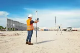 Eine Person mit Sicherheitsausrüstung verwendet auf einer Baustelle ein Lasernivelliergerät.