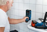 Eine Person scannt in einem Arbeitsbereich eine geflieste Wand mit einem Inspektionswerkzeug.