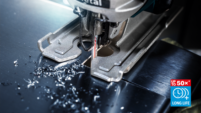 Eine Stichsäge schneidet durch ein Metallblech, Metallspäne sind auf der Oberfläche verstreut.