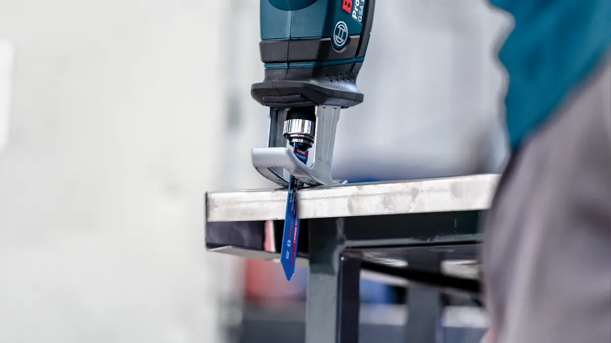 Eine Person mit Sicherheitsausrüstung schneidet mit einer Säbelsäge ein Metallblech.