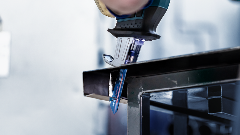 Person, die mit einer Stichsäge einen Metallträger schneidet.