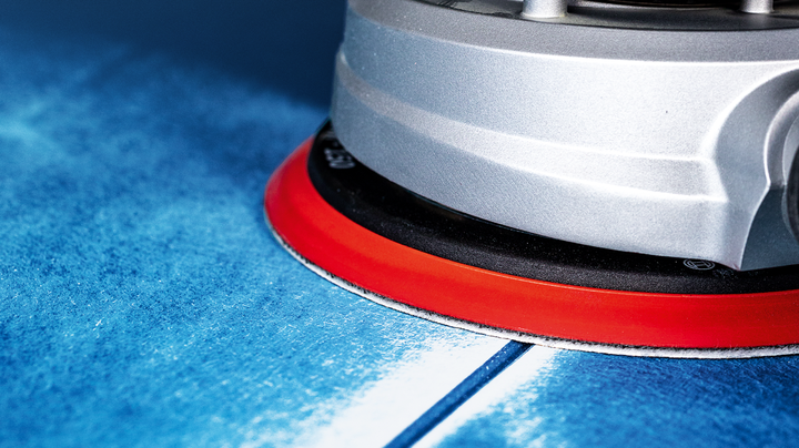 Elektrowerkzeug mit roter Basis zum Schleifen einer blauen Oberfläche.