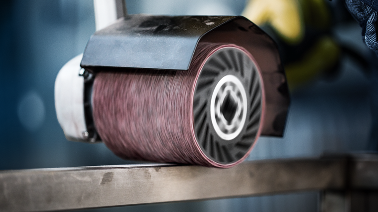 Eine Person mit Schutzausrüstung schleift eine Metalloberfläche mit einem großen Schleifwerkzeug.