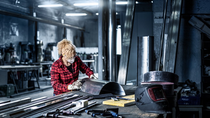 Person mit Sicherheitsausrüstung formt in einer Werkstatt ein Metallblech.