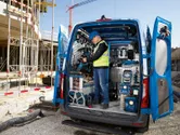 Eine Person in Sicherheitsausrüstung räumt auf einer Baustelle Elektrowerkzeuge in einem Lieferwagen ein.