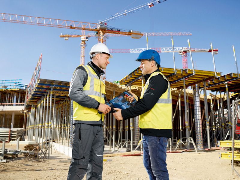 Zwei Personen in Sicherheitsausrüstung besprechen auf einer Baustelle ein Elektrowerkzeug.