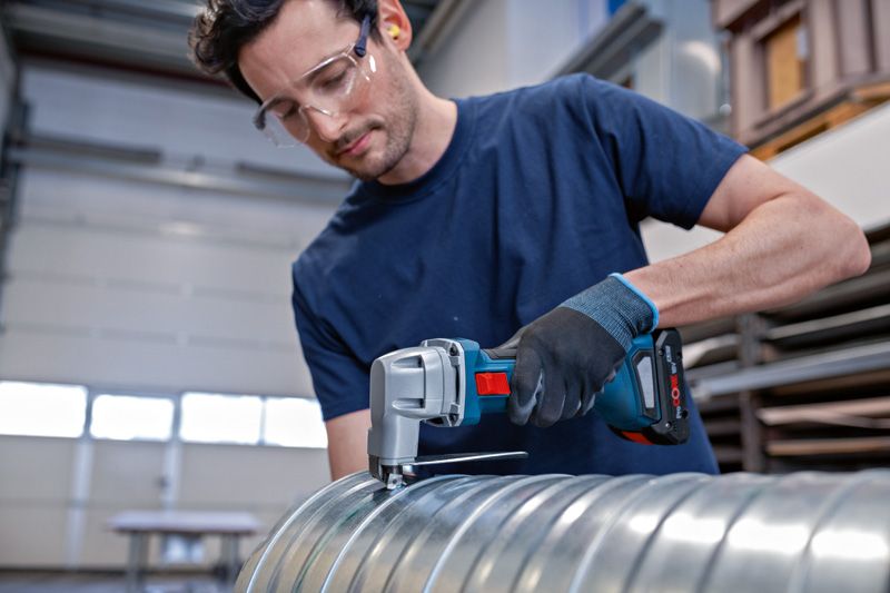 Eine Person mit Sicherheitsausrüstung schneidet mit einer kabellosen Metallschere einen Metallkanal durch.