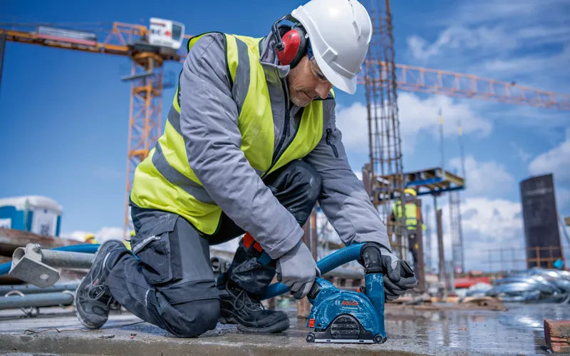 Eine Person mit Sicherheitsausrüstung verwendet einen Akku-Winkelschleifer auf einer Betonoberfläche.