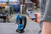 Eine Person stellt in einer Werkstatt per Smartphone eine Akku-Stichsäge ein.