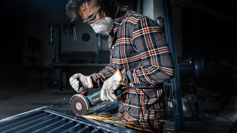 Eine Person mit Sicherheitsausrüstung schleift Metall und erzeugt Funken.