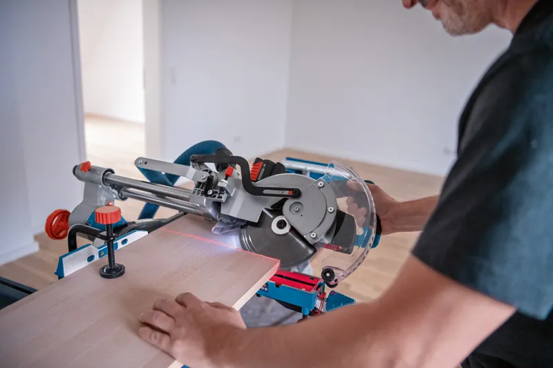 Eine Person verwendet eine kabellose Gehrungssäge mit einem Lasernivellierungswerkzeug, um Holz zu schneiden.