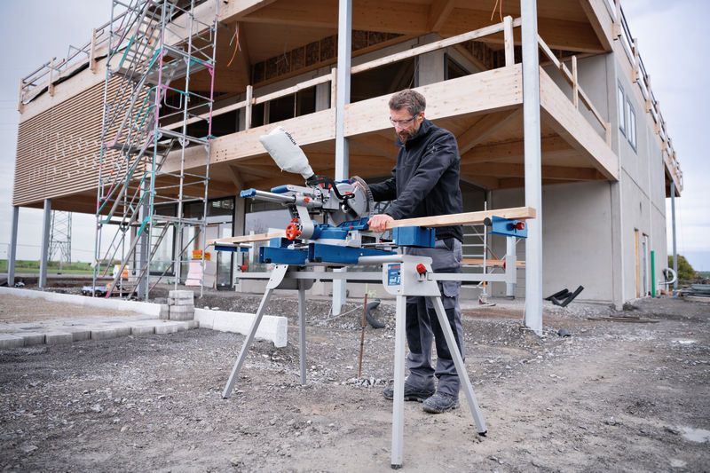 Eine Person mit Sicherheitsausrüstung schneidet auf einer Baustelle Holz mit einer Akku-Gehrungssäge.