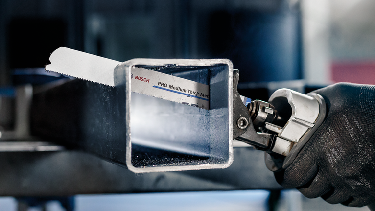 Person mit Sicherheitsausrüstung, die mit einer Säbelsäge ein Metallrohr durchtrennt.