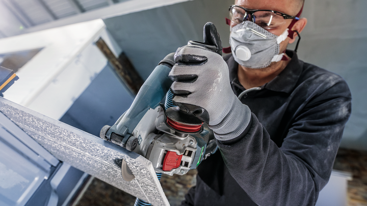 Eine Person mit Sicherheitsausrüstung schneidet mit einem Elektrowerkzeug eine Metallplatte.